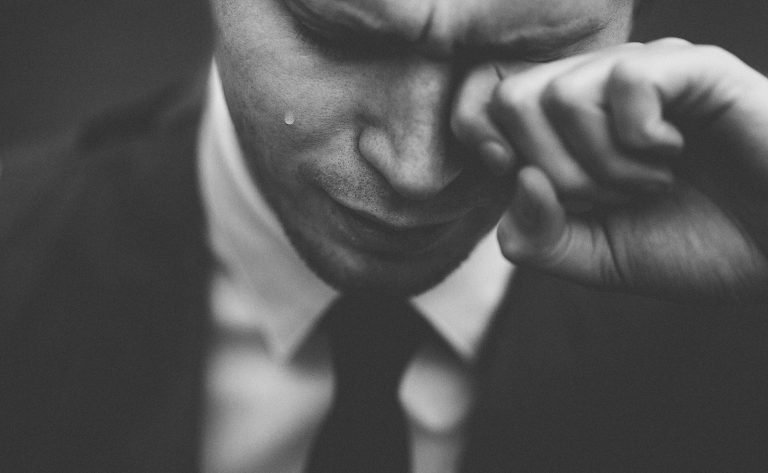 Person with a tear on their check, knuckle to their eye. Picture for blog on The Lasting Impact of Childhood Bullying on Adult Mental Health
